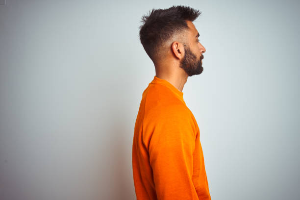 istock Young indian man wearing orange sweater over isolated white background looking to side, relax profile pose with natural face with confident smile. 1205740877