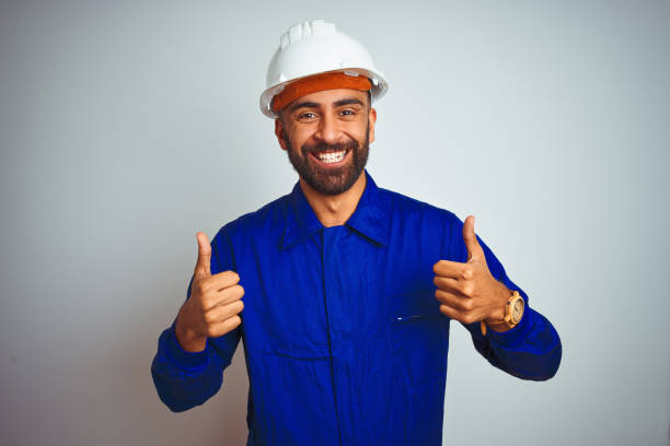 istock Handsome indian worker man wearing uniform and helmet over isolated white background success sign doing positive gesture with hand, thumbs up smiling and happy. Cheerful expression and winner gesture. 1205740926