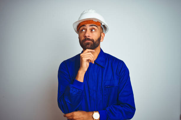 красивый индийский рабочий мужчина в форме и шлеме на изолированном белом фоне с рукой на подбородке думает о вопросе, задумчивом выражени� - reflective workwear стоковые фото и изображения