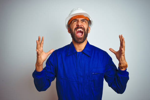 istock Handsome indian worker man wearing uniform and helmet over isolated white background crazy and mad shouting and yelling with aggressive expression and arms raised. Frustration concept. 1205740977
