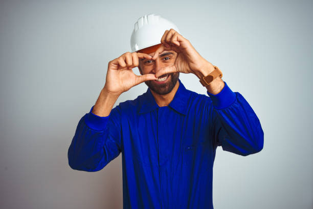 istock Handsome indian worker man wearing uniform and helmet over isolated white background smiling in love doing heart symbol shape with hands. Romantic concept. 1205741147