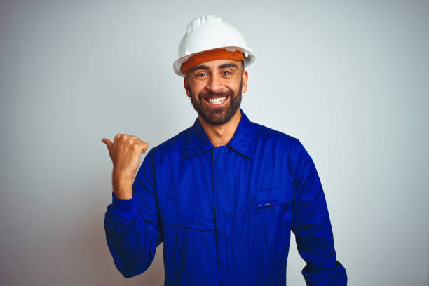 istock Handsome indian worker man wearing uniform and helmet over isolated white background smiling with happy face looking and pointing to the side with thumb up. 1205741176