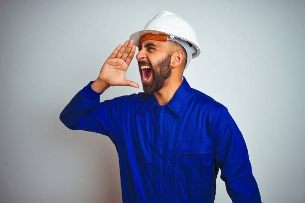 istock Handsome indian worker man wearing uniform and helmet over isolated white background shouting and screaming loud to side with hand on mouth. Communication concept. 1205741215