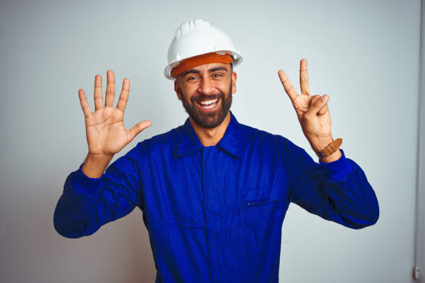 istock Handsome indian worker man wearing uniform and helmet over isolated white background showing and pointing up with fingers number seven while smiling confident and happy. 1205741380