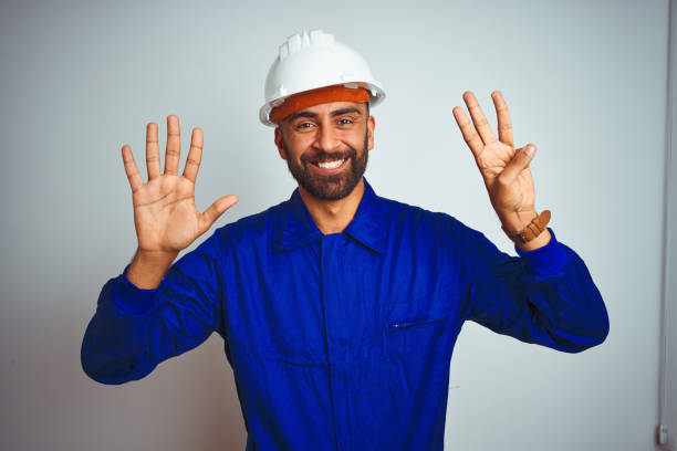 istock Handsome indian worker man wearing uniform and helmet over isolated white background showing and pointing up with fingers number eight while smiling confident and happy. 1205741383