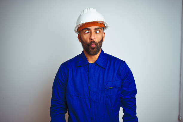 istock Handsome indian worker man wearing uniform and helmet over isolated white background making fish face with lips, crazy and comical gesture. Funny expression. 1205741396