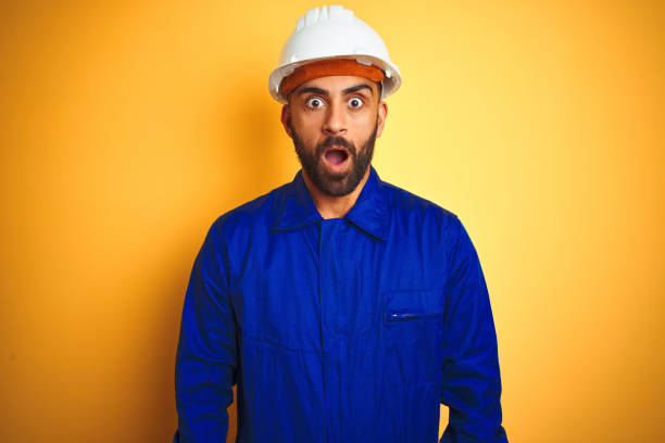istock Handsome indian worker man wearing uniform and helmet over isolated yellow background afraid and shocked with surprise expression, fear and excited face. 1205741427