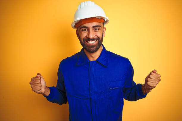 istock Handsome indian worker man wearing uniform and helmet over isolated yellow background celebrating surprised and amazed for success with arms raised and open eyes. Winner concept. 1205741504
