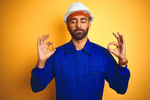 istock Handsome indian worker man wearing uniform and helmet over isolated yellow background relax and smiling with eyes closed doing meditation gesture with fingers. Yoga concept. 1205741533