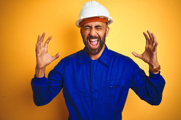 istock Handsome indian worker man wearing uniform and helmet over isolated yellow background celebrating mad and crazy for success with arms raised and closed eyes screaming excited. Winner concept 1205741612