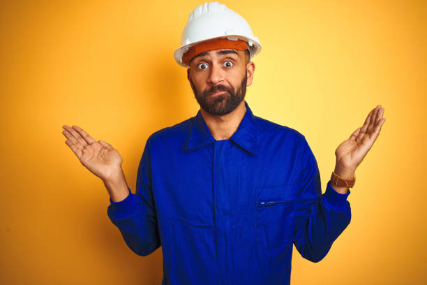 istock Handsome indian worker man wearing uniform and helmet over isolated yellow background clueless and confused expression with arms and hands raised. Doubt concept. 1205741689