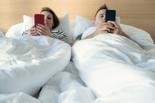 istock Young married couple using their mobile phone in bed ignoring each other as strangers. Relationship and communication problems and internet social network addiction 1205744544