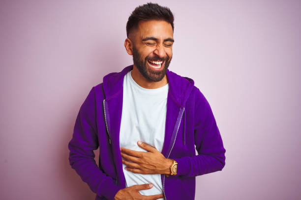 Young indian man wearing purple sweatshirt standing over isolated pink background smiling and laughing hard out loud because funny crazy joke with hands on body. Young indian man wearing purple sweatshirt standing over isolated pink background smiling and laughing hard out loud because funny crazy joke with hands on body. people laughing hard stock pictures, royalty-free photos & images