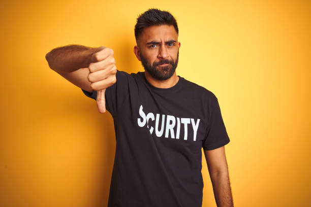 istock Arab indian hispanic safeguard man wearing security uniform over isolated yellow background looking unhappy and angry showing rejection and negative with thumbs down gesture. Bad expression. 1205745446