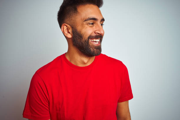 młody indyjski mężczyzna ubrany w czerwoną koszulkę na odizolowanym białym tle, patrząc z uśmiechem na twarzy, naturalną ekspresją. śmiejąc się pewnie. - t shirt men red portrait zdjęcia i obrazy z banku zdjęć