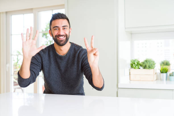 schöner hispanischer mann trägt lässigen pullover zu hause zeigt und zeigt mit den fingern nummer sieben, während lächelnd zuversichtlich und glücklich. - hispanic male stock-fotos und bilder