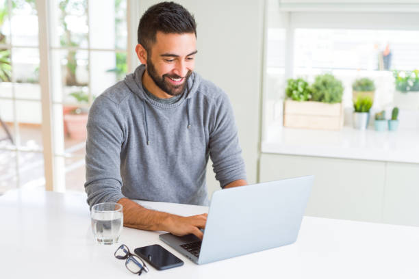 homme hispanique bel travaillant utilisant l’ordinateur portatif d’ordinateur avec un visage heureux restant et souriant avec un sourire confiant affichant des dents - toothy smile relaxation white healthcare and medicine photos et images de collection