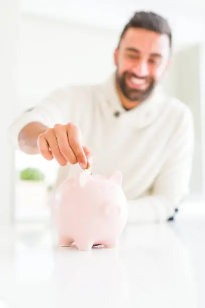 Photo of Man smiling putting a coin inside of piggy bank saving for investment