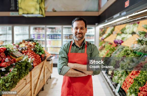 Confident Mature Employee In Supermarket Wearing Red Apron Stock Photo - Download Image Now