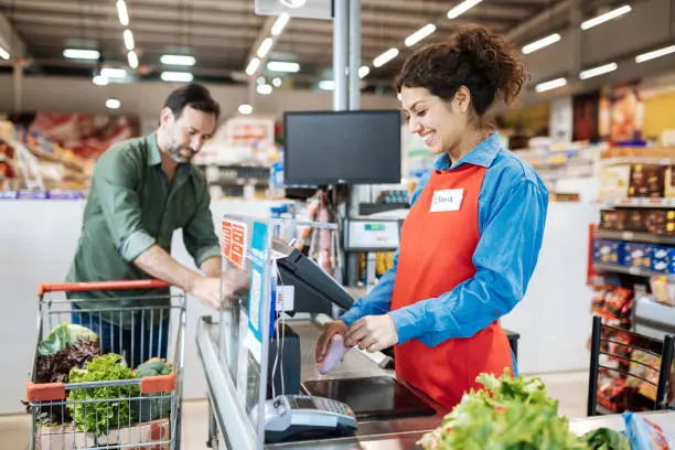 Photo of Employee at cash register in supermarket, serving the customer