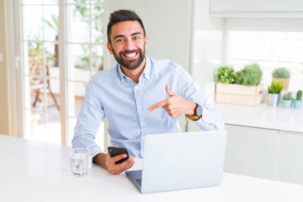 istock Handsome hispanic business man using laptop and smartphone very happy pointing with hand and finger 1205749789