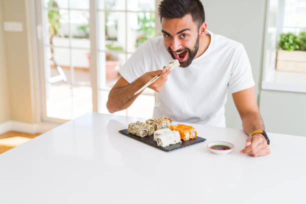 istock Handsome man smiling happy enjoying eating fresh colorful asian sushi using chopsticks 1205750856