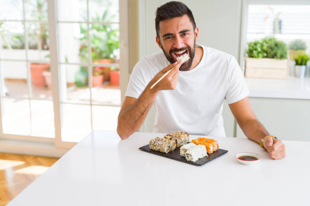 istock Handsome man smiling happy enjoying eating fresh colorful asian sushi using chopsticks 1205751100