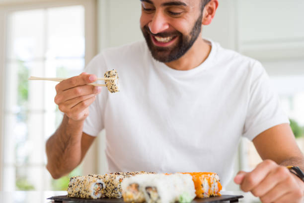 istock Handsome man smiling happy enjoying eating fresh colorful asian sushi using chopsticks 1205751368