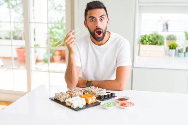 istock Handsome hispanic man eating asian sushi using chopsticks scared in shock with a surprise face, afraid and excited with fear expression 1205751391