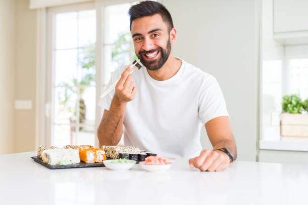 istock Handsome man smiling happy enjoying eating fresh colorful asian sushi using chopsticks 1205751392