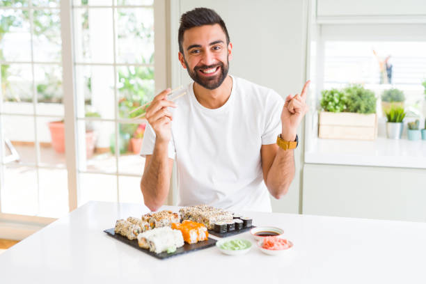 istock Handsome hispanic man eating asian sushi using chopsticks very happy pointing with hand and finger to the side 1205751394