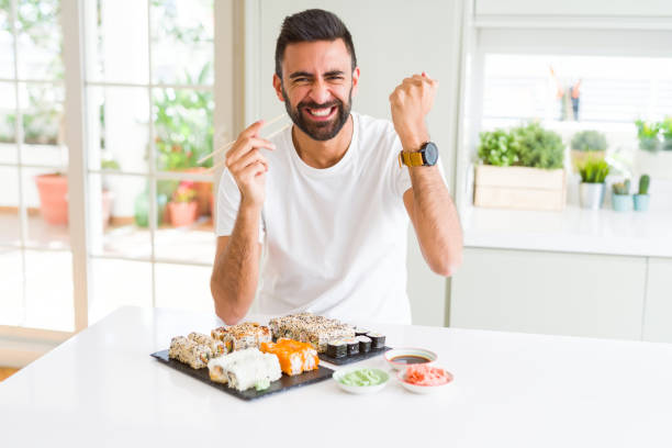 istock Handsome hispanic man eating asian sushi using chopsticks annoyed and frustrated shouting with anger, crazy and yelling with raised hand, anger concept 1205751398
