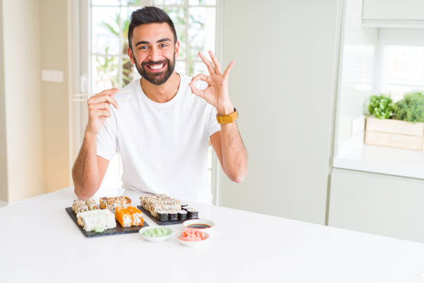istock Handsome hispanic man eating asian sushi using chopsticks doing ok sign with fingers, excellent symbol 1205751404