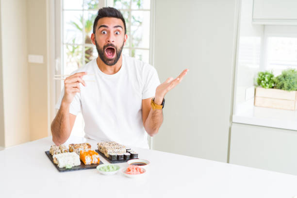 istock Handsome hispanic man eating asian sushi using chopsticks very happy and excited, winner expression celebrating victory screaming with big smile and raised hands 1205751410