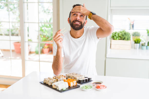 istock Handsome hispanic man eating asian sushi using chopsticks stressed with hand on head, shocked with shame and surprise face, angry and frustrated. Fear and upset for mistake. 1205751414