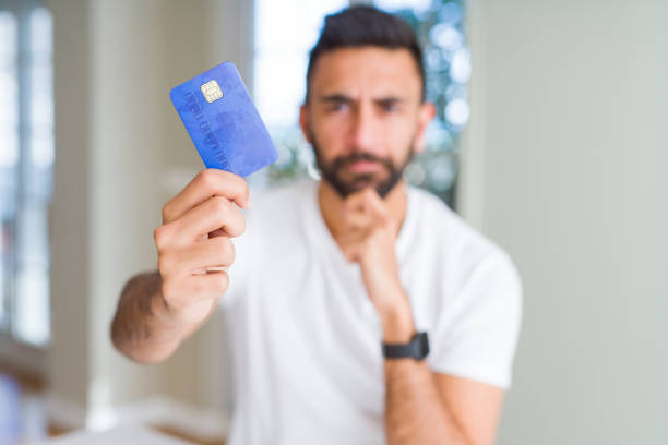 istock Handsome hispanic man holding credit card serious face thinking about question, very confused idea 1205751683