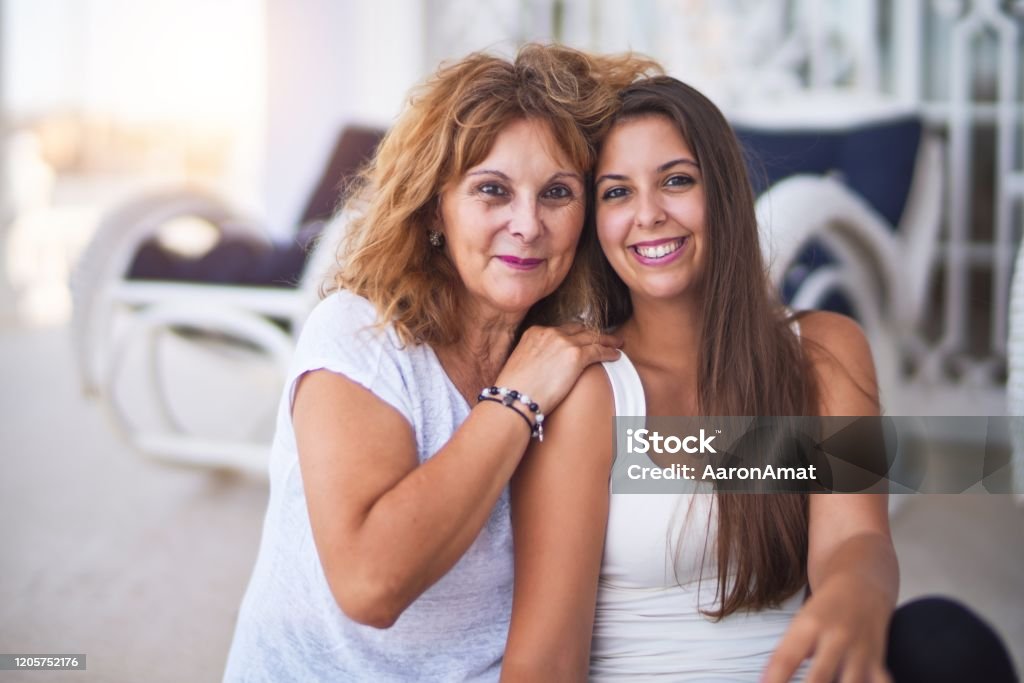 Beautiful mother and daugther sitting at terrace hugging and smiling Mother Stock Photo