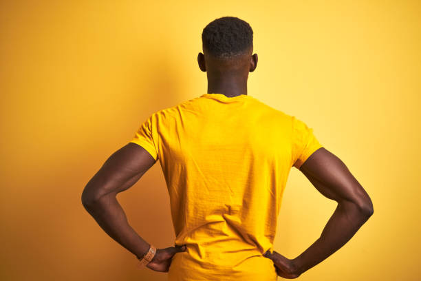 jovem afro-americano vestindo camiseta casual em pé sobre fundo amarelo isolado parado para trás olhando para o outro lado com os braços no corpo - back to the wall - fotografias e filmes do acervo