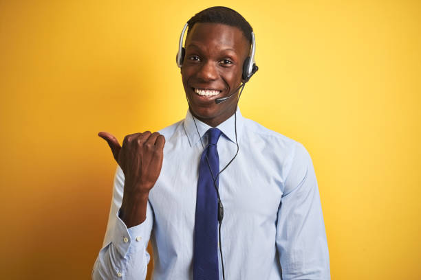 istock African american operator man working using headset over isolated yellow background smiling with happy face looking and pointing to the side with thumb up. 1205752498