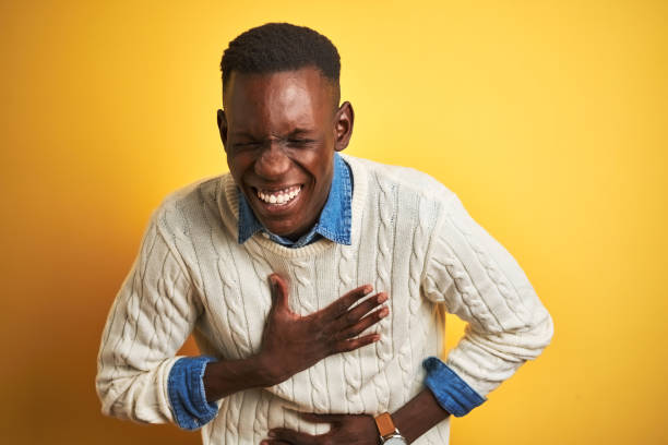 African american man wearing denim shirt and white sweater over isolated yellow background smiling and laughing hard out loud because funny crazy joke with hands on body. African american man wearing denim shirt and white sweater over isolated yellow background smiling and laughing hard out loud because funny crazy joke with hands on body. people laughing hard stock pictures, royalty-free photos & images