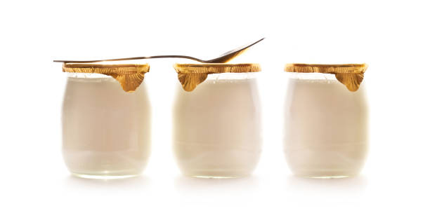Three plain yogurts in glass jars and a spoon isolated on white background