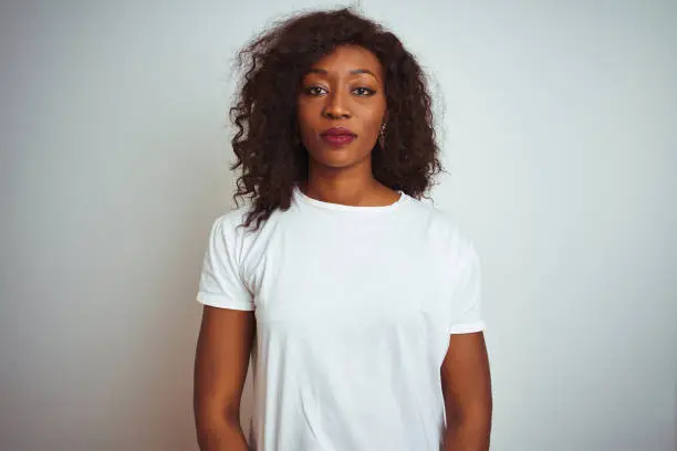 Photo of Young african american woman wearing t-shirt standing over isolated white background Relaxed with serious expression on face. Simple and natural looking at the camera.