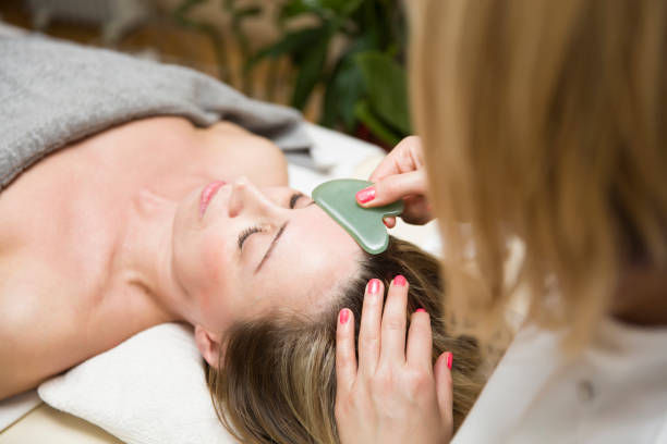 mulher fazendo uma massagem facial gua sha com massageador de pedra de jade natural - spooning - fotografias e filmes do acervo