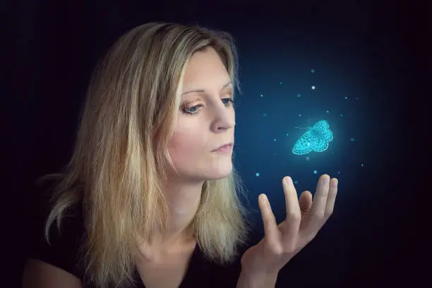 Beauty young blond hair woman hold hand under glowing blue butterfly. Photomanipulation glowing lepidopteran on black background