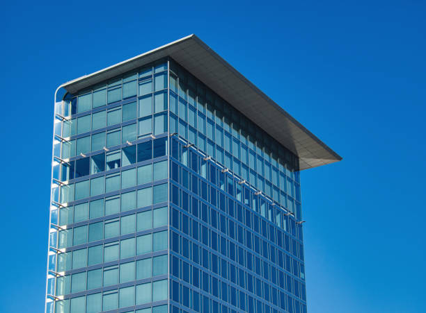 A narrow high-rise building with glass front and projecting flat roof