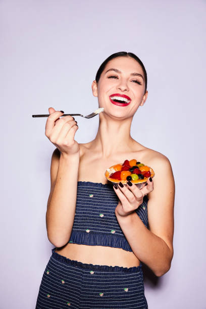 istock Laughing young woman eating a delicious mixed fruit tart 1205767094