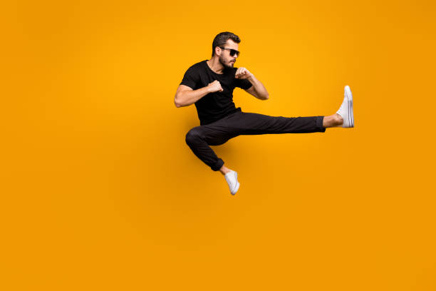 istock Full length photo of handsome guy jumping high practicing self defense kicking confident facial expression wear sun specs black t-shirt pants isolated yellow color background 1205773983