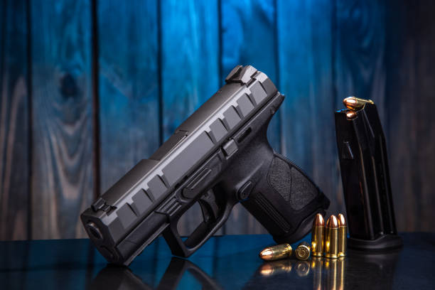 istock Black modern gun and ammunition for it on dark blue background. Short-barreled weapons for sports and self-defense. Armament for police units, special forces and the army. 1205775677