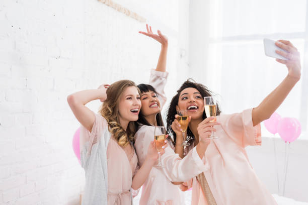 podekscytowany wielokulturowe dziewczyny z kieliszkami szampana robienia selfie na smartfonie podczas piżamy strony - bachelorette party zdjęcia i obrazy z banku zdjęć