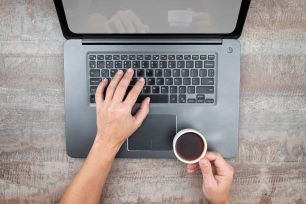 istock Hands holding a cup of coffee while typing on a laptop 1205778872